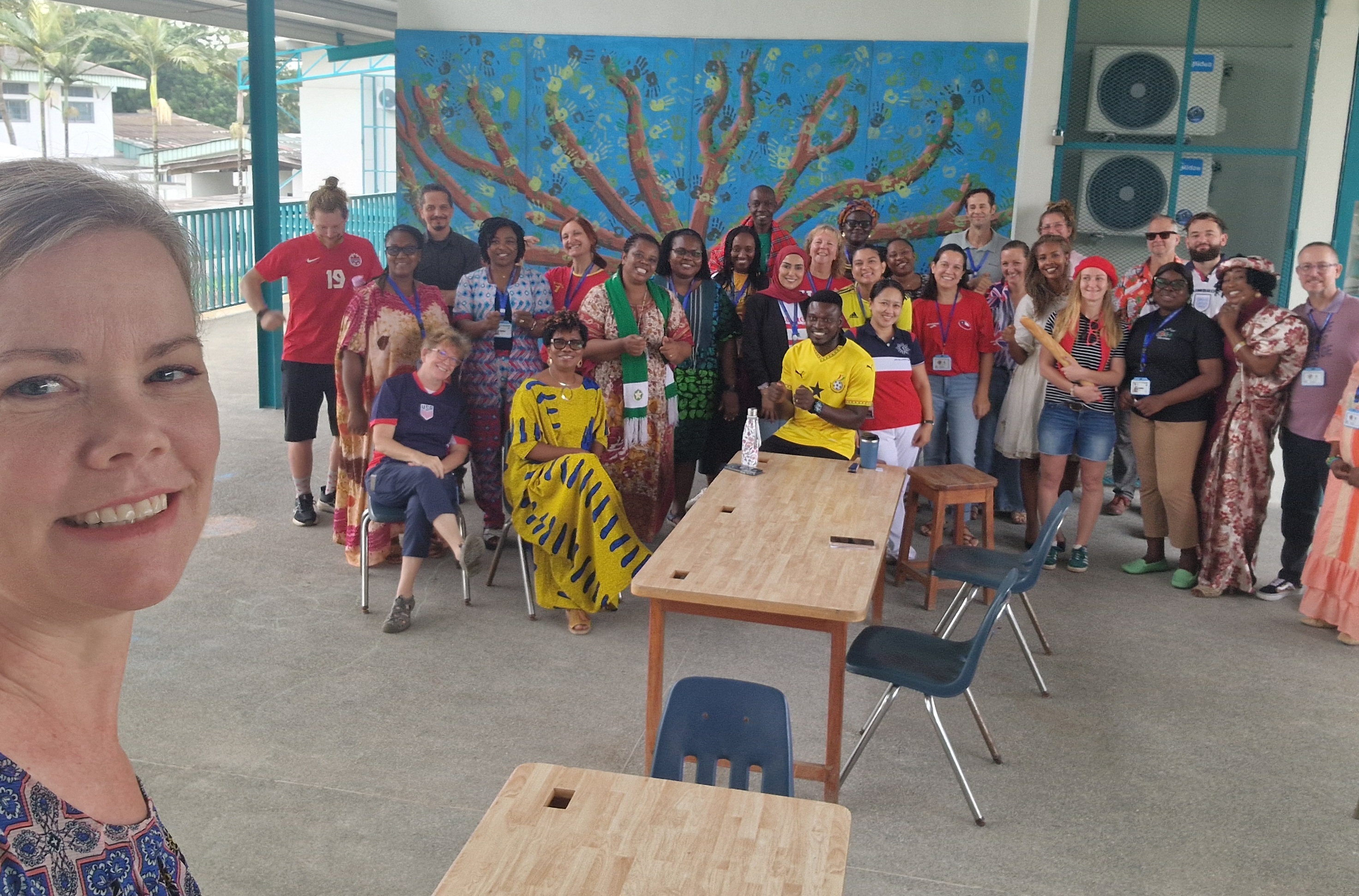 Diverse group photo with colorful tree mural, taken at conference or workshop