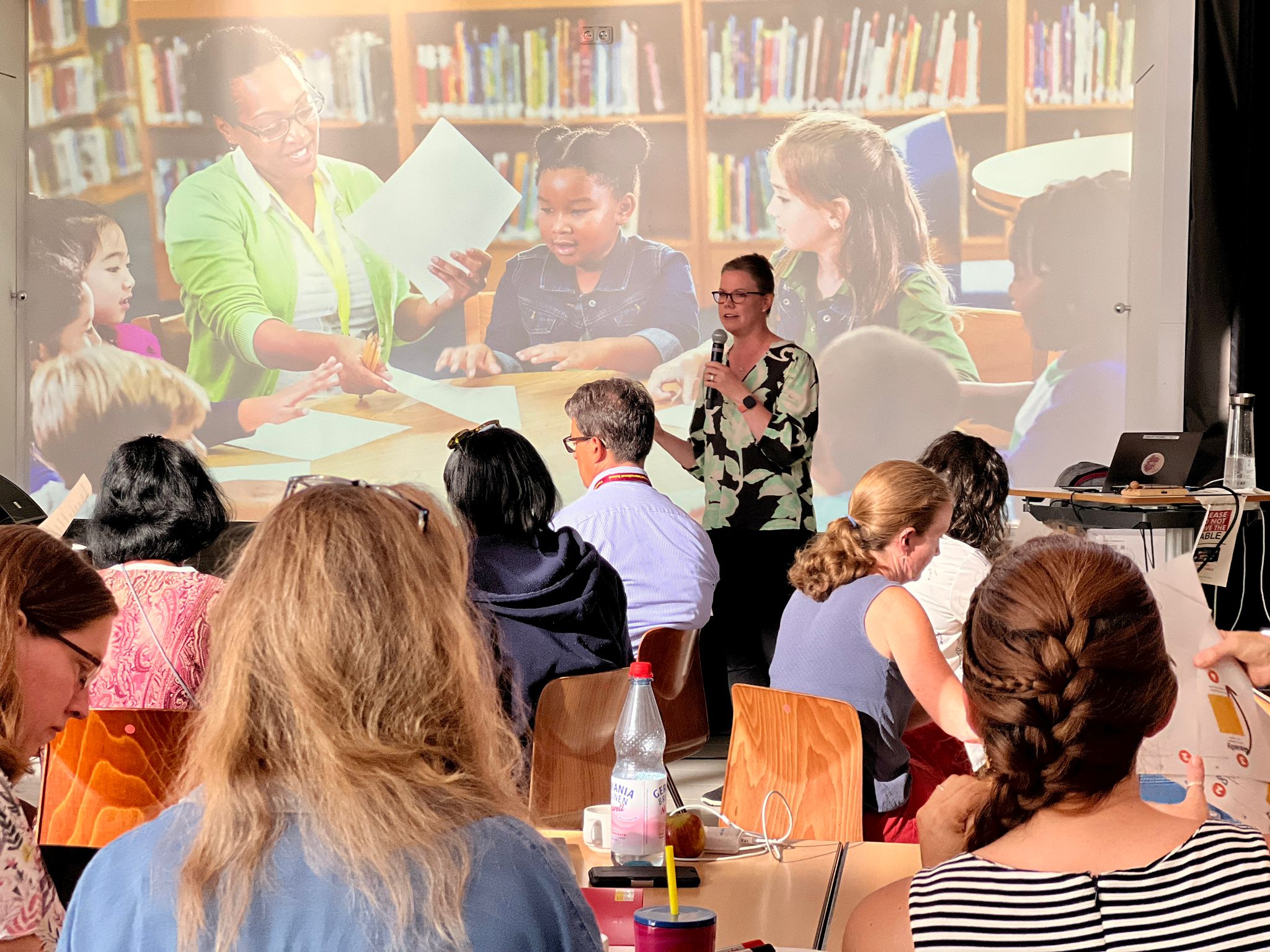 Presenter speaking about classroom learning with children's image projected behind