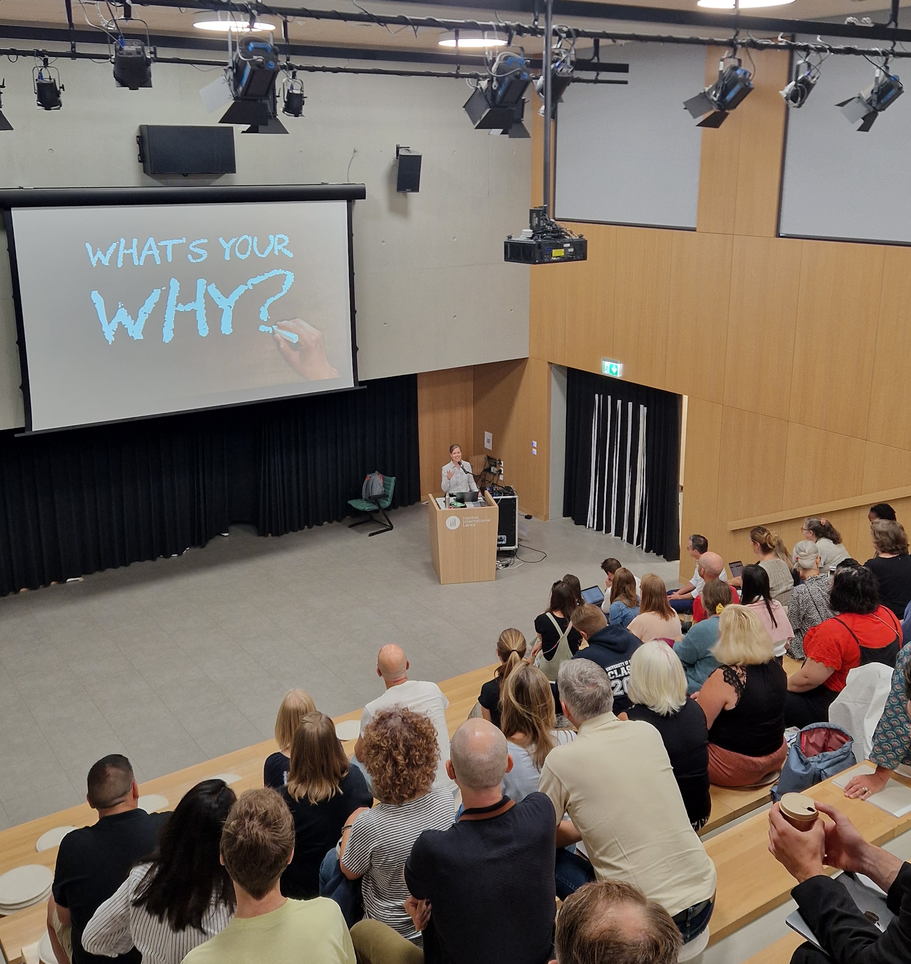Presenter asking "What's your why?" to a full lecture hall audience