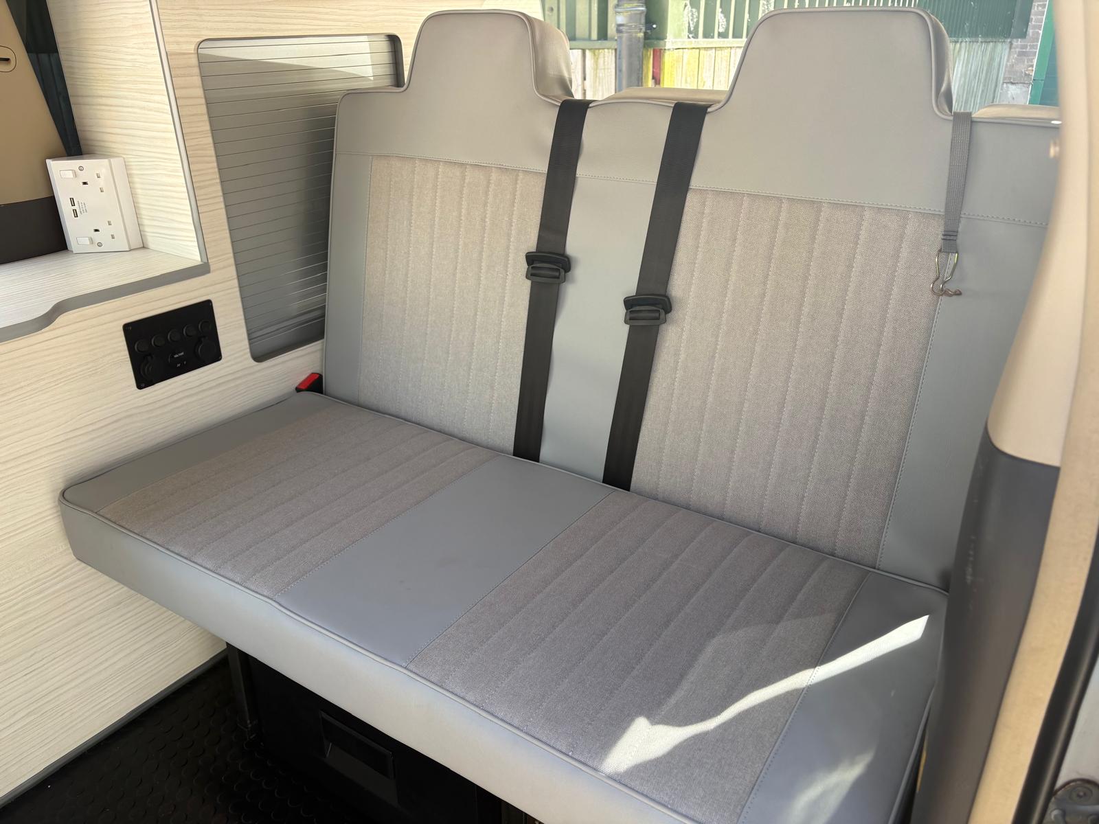 Light gray fabric and leather bench seat with two black seat belts in a vehicle interior.