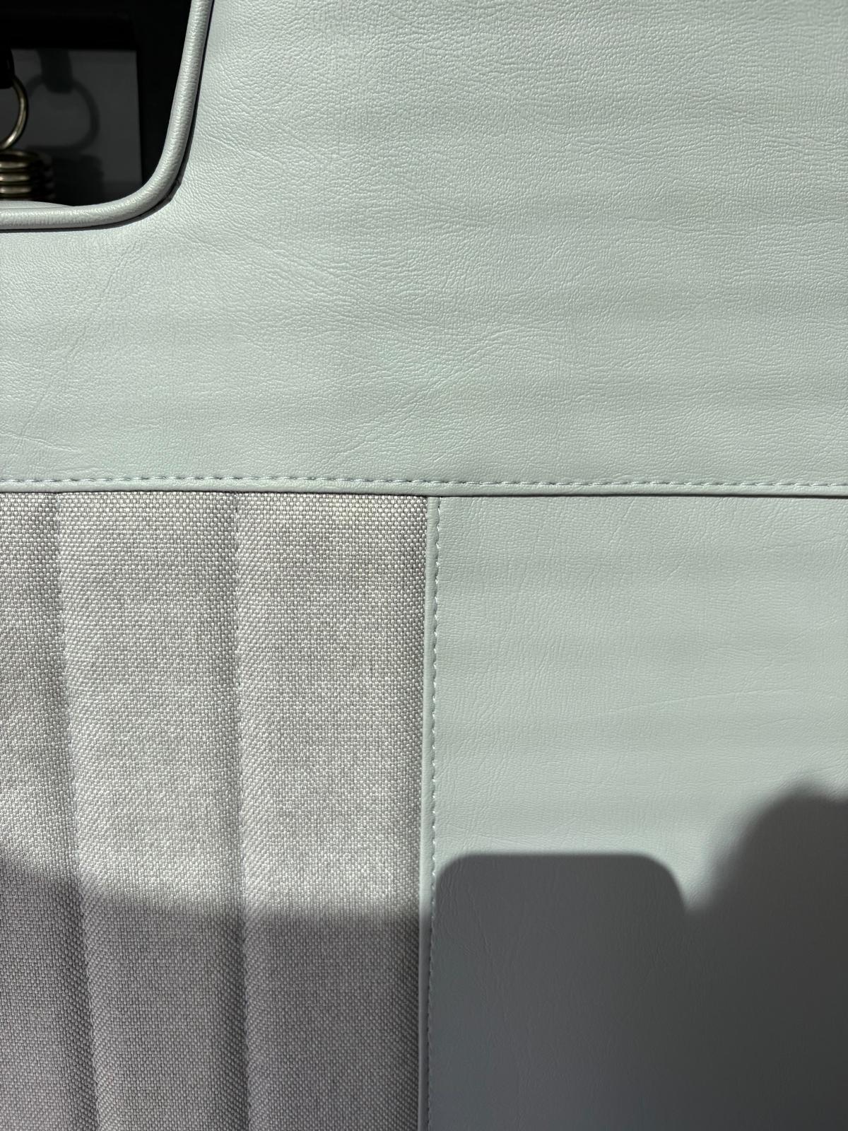 Close-up of textured light gray leather and fabric upholstery with visible stitching.