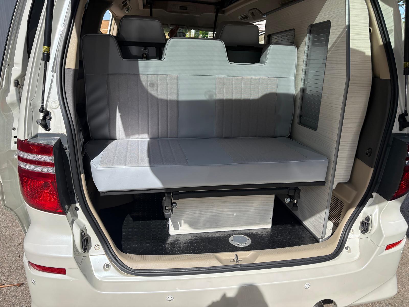 Rear view of a white van with an open hatch showing a gray foldable bench seat inside.