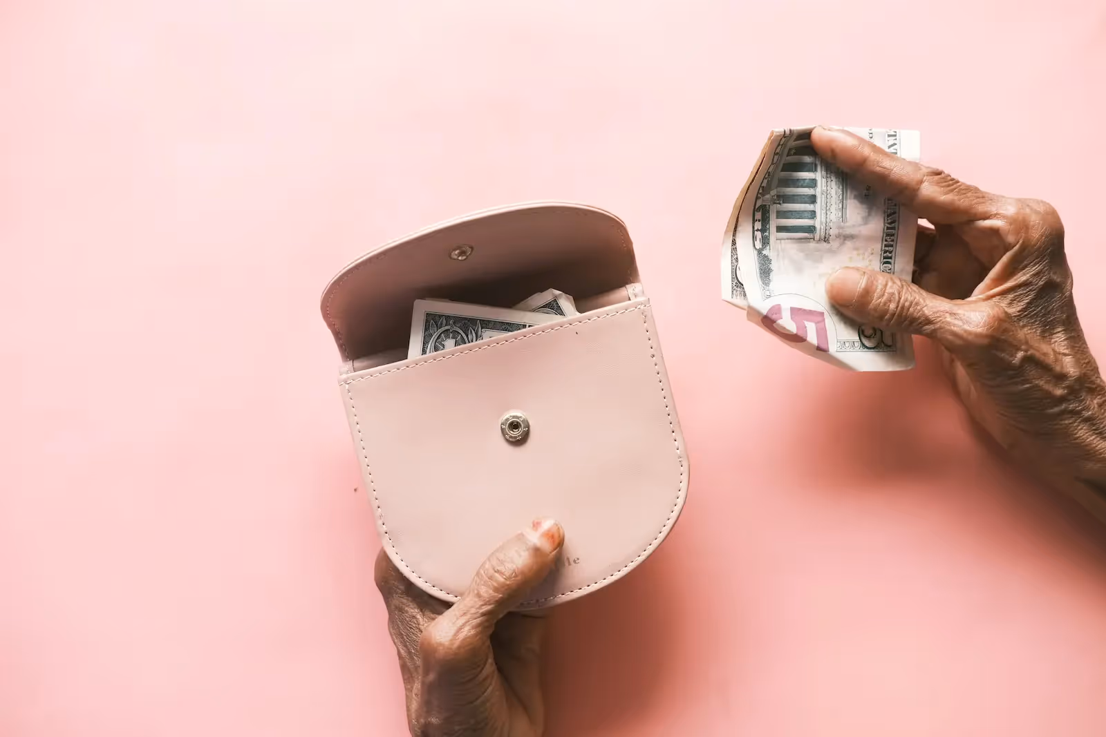 Pink wallet with money inside and a hand holding a paper bill
