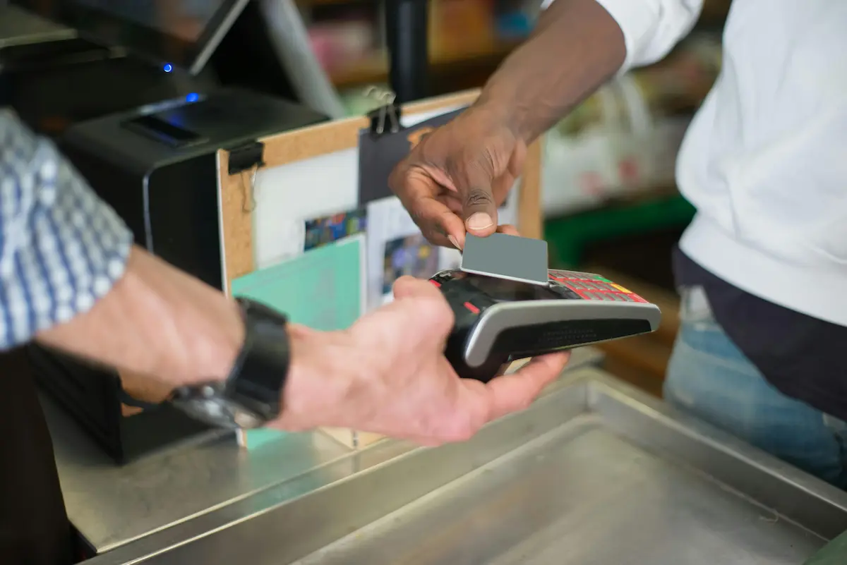 Person tapping a credit card at a pharmacy counter to earn rewards on an HSA-eligible purchase