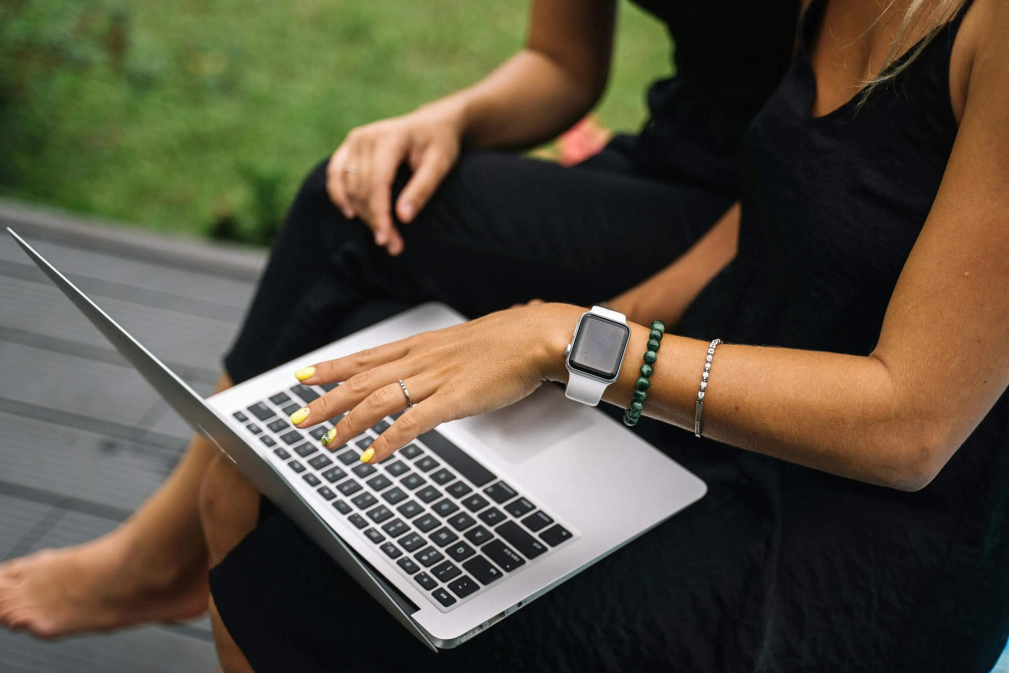 Woman shopping online on a laptop, wearing an Apple Watch and jewelry, outdoors
