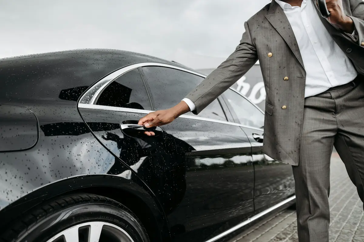 Professional chauffeur in suit opening the door of a luxury black vehicle, representing the Citi Strata Elite Blacklane credit benefit in 2026