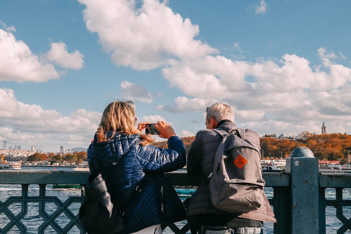 Two travelers photographing a waterfront city skyline representing Capital One Venture X travel credit benefits