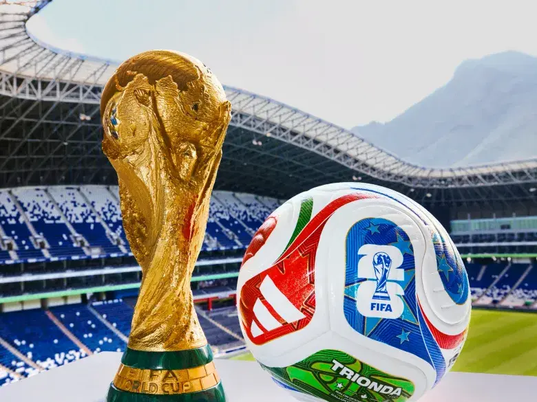 FIFA World Cup trophy and official match ball displayed in front of a stadium