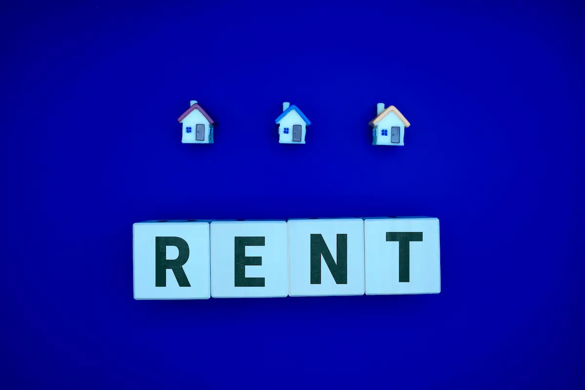 Wooden tiles spelling "RENT" beneath three small house figures on a blue background
