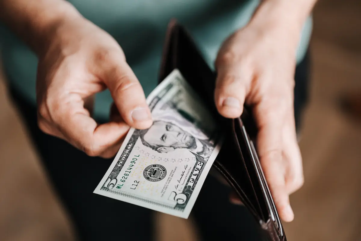 Close-up of two hands pulling a five dollar bill out of a black wallet