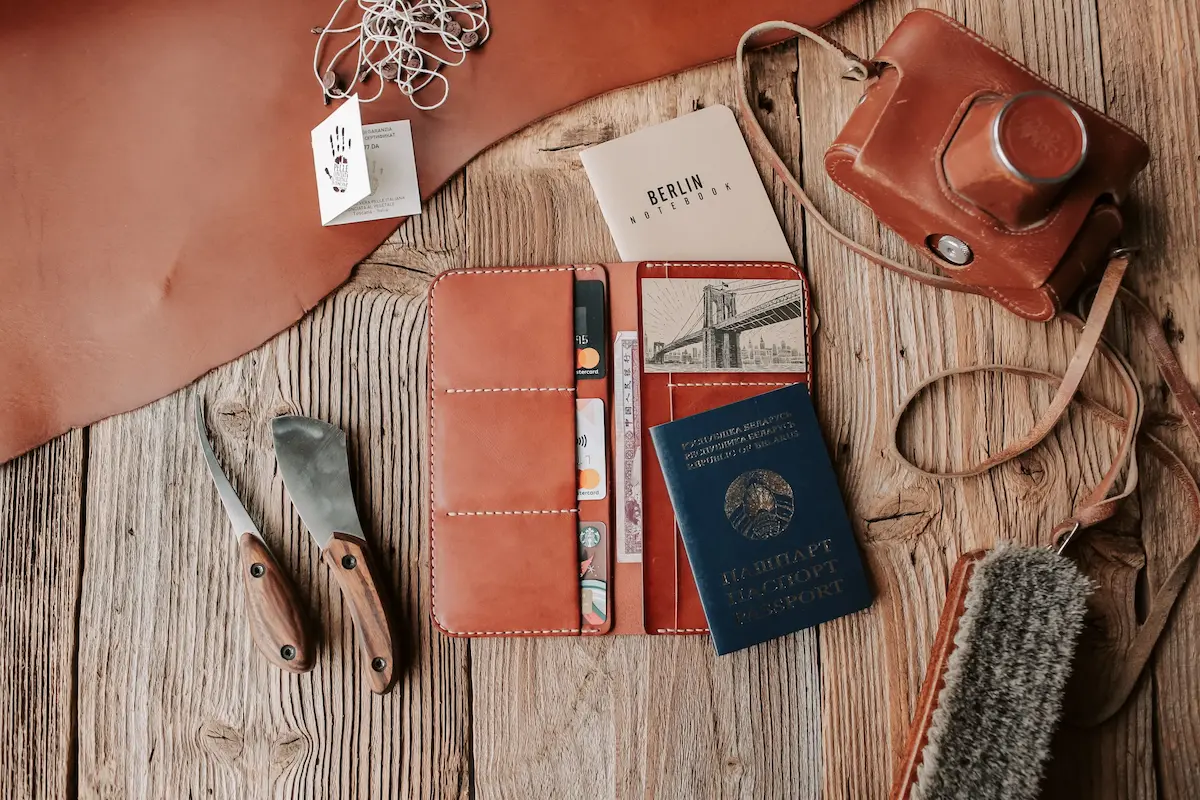 Open leather travel wallet with a credit card, notebook, and postcard illustration arranged on a rustic wooden table