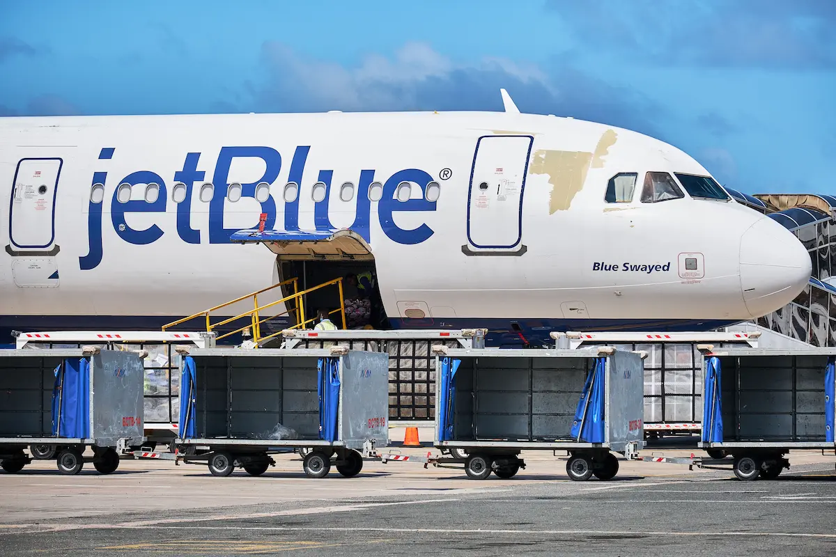 Airplane parked at the gate with baggage carts lined up on the tarmac under a blue sky