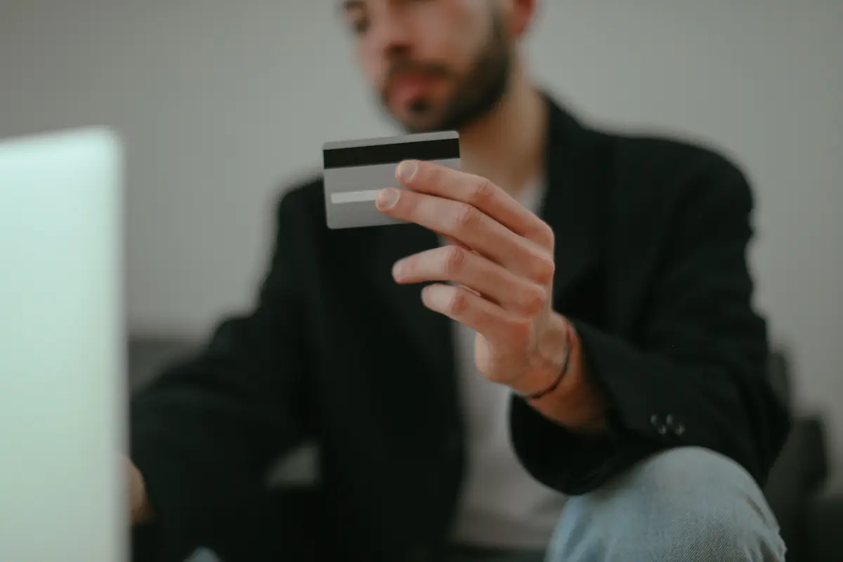 Man holding a blank credit card up to check the details while sitting in front of an open laptop