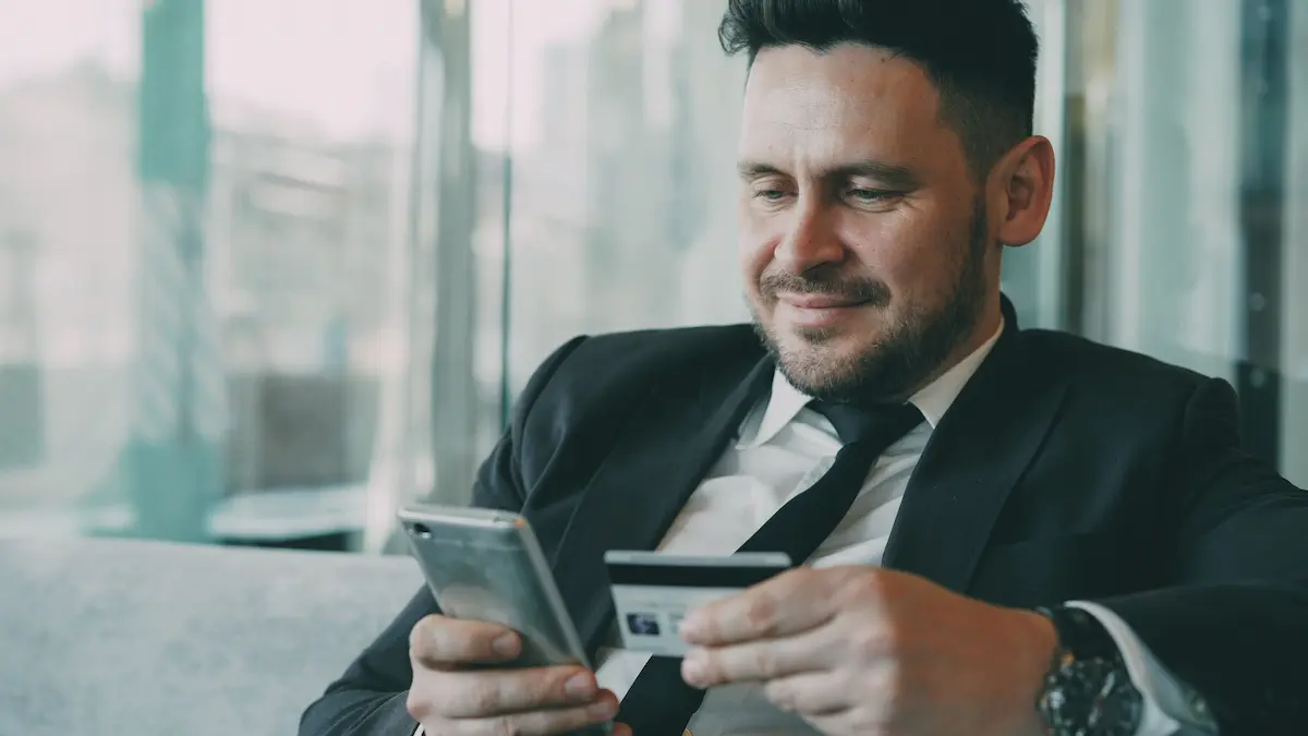 Businessman reviewing his credit card details on his phone, representing a cardholder deciding whether to keep or downgrade after an annual fee increase