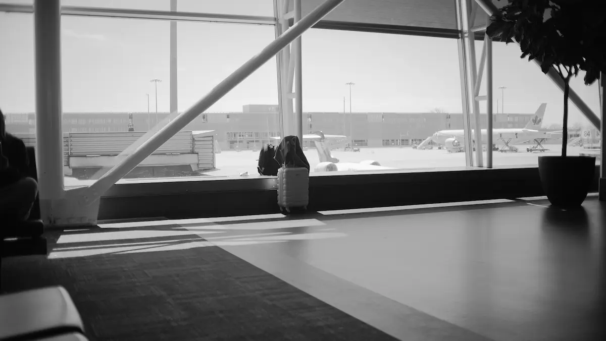 Black-and-white photo of a quiet airport terminal window ledge with a suitcase, representing narrowing lounge access for travelers