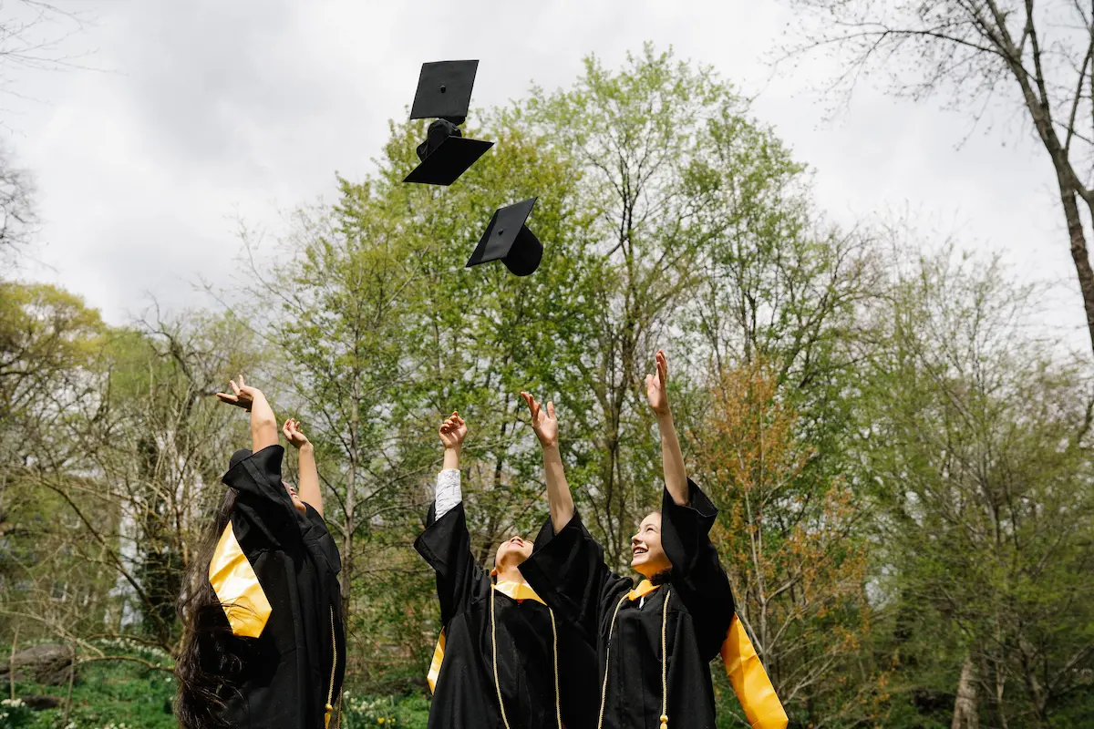 Recent graduates in caps and gowns tossing their graduation caps into the air