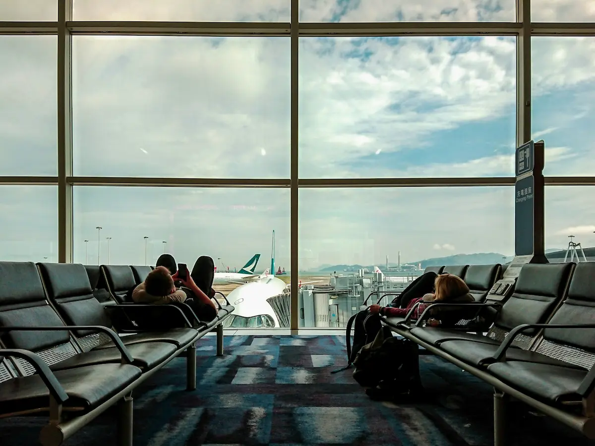 Travelers relaxing in airport gate seating with a view of the tarmac, representing time spent waiting between flights