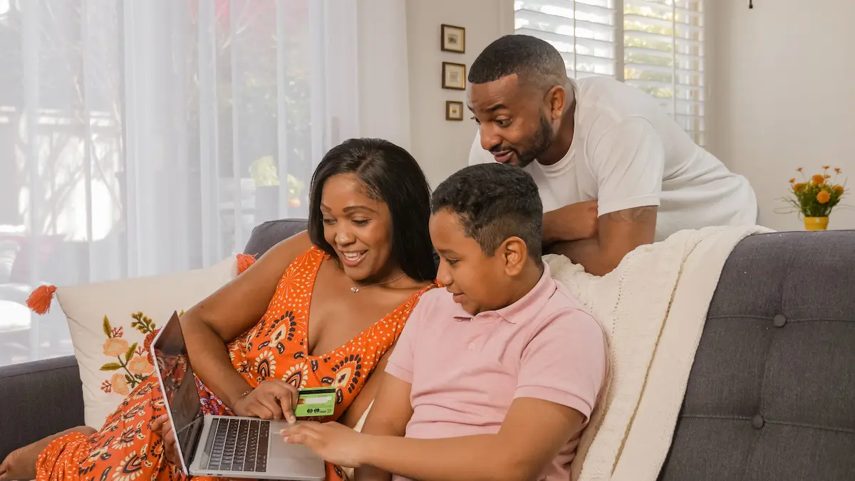 Family sitting together on a couch using a laptop and credit card to shop online