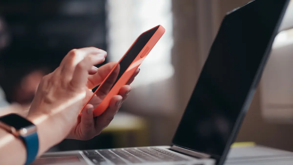 Close-up of a hand holding a smartphone next to an open laptop