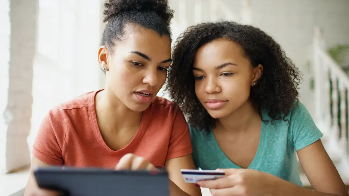 Two women reviewing a credit card and tablet together, comparing cash back card options.