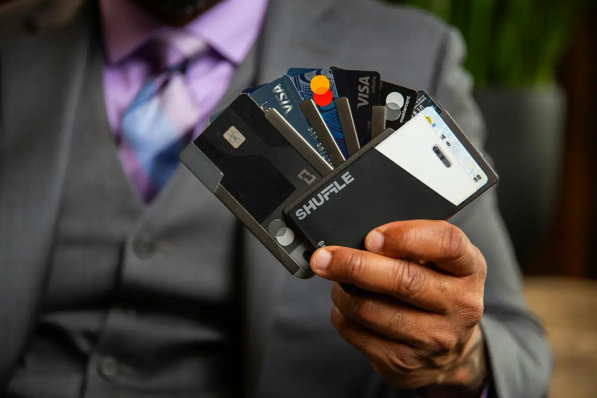 Man in a suit holding a wallet fanned out with multiple credit cards, including Visa and Mastercard, representing a credit card rewards stacking strategy