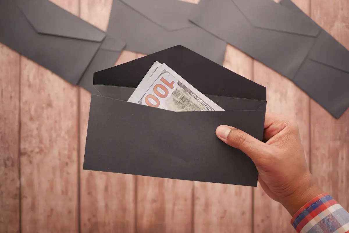 Hand holding a black envelope with hundred dollar bills inside