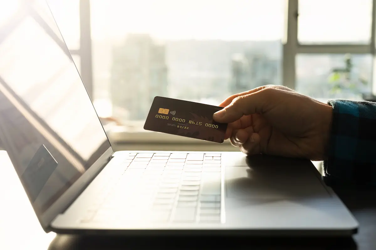 Hand holding a black premium credit card near a laptop.