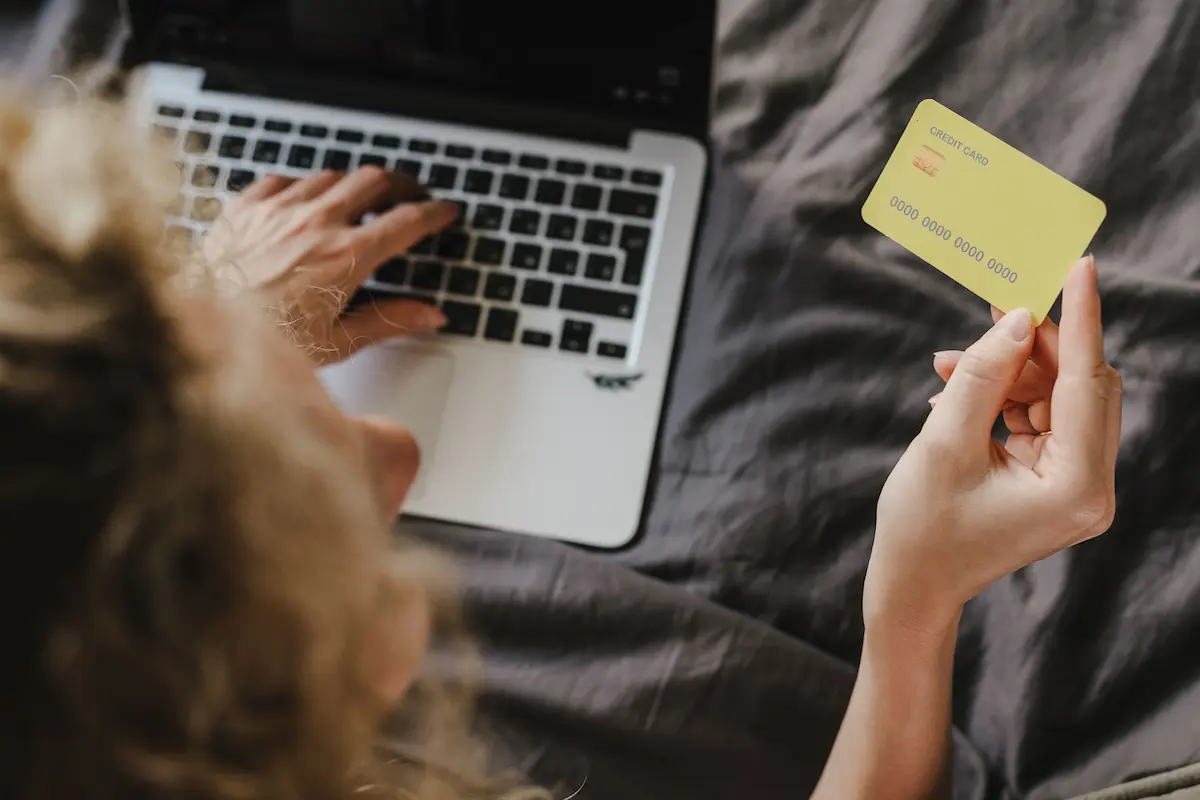 Person typing on a laptop while holding a yellow credit card