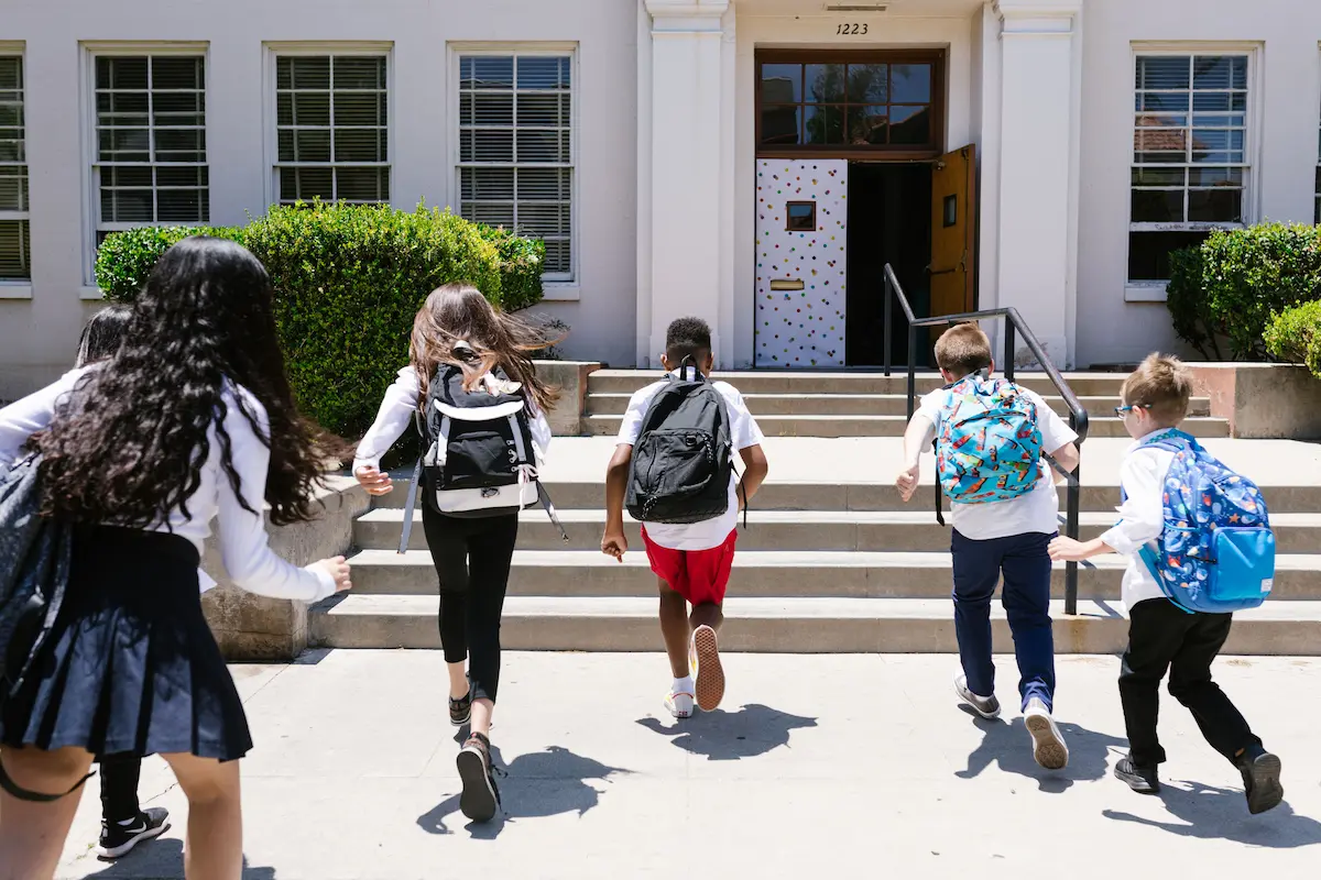 Students with backpacks walking up steps into a school building