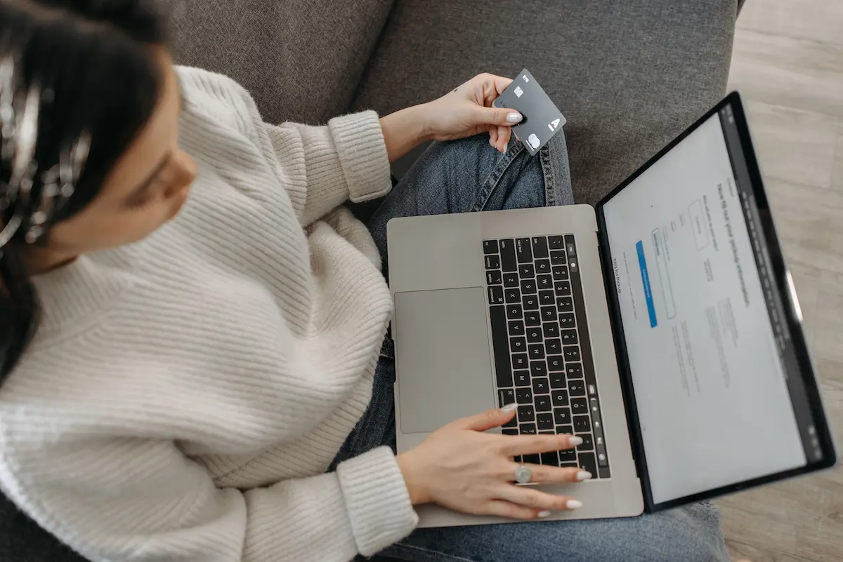 Person holding a credit card while using a laptop showing an application form