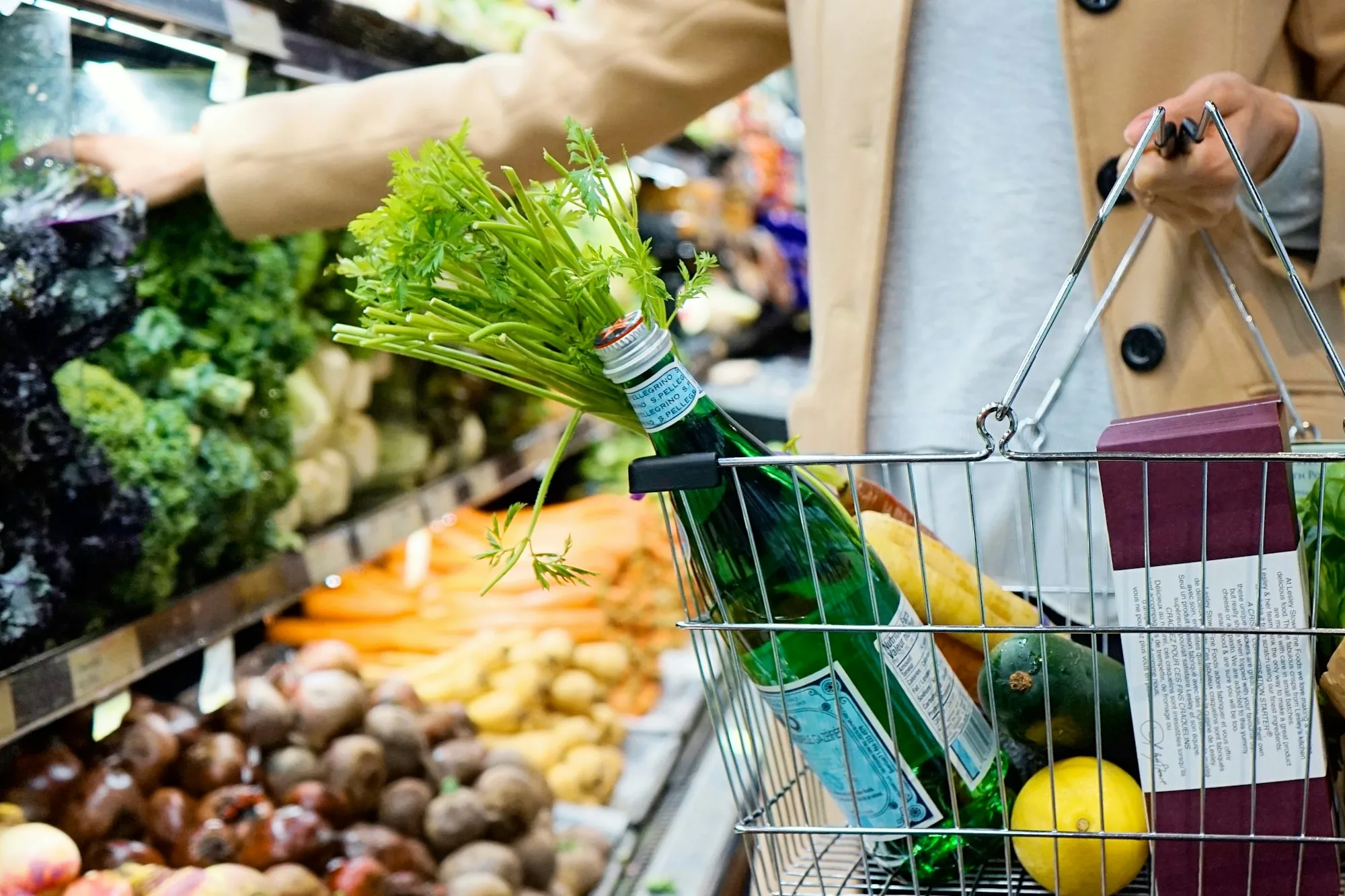 Shopper picking fresh produce with a basket of groceries in a supermarket aisle