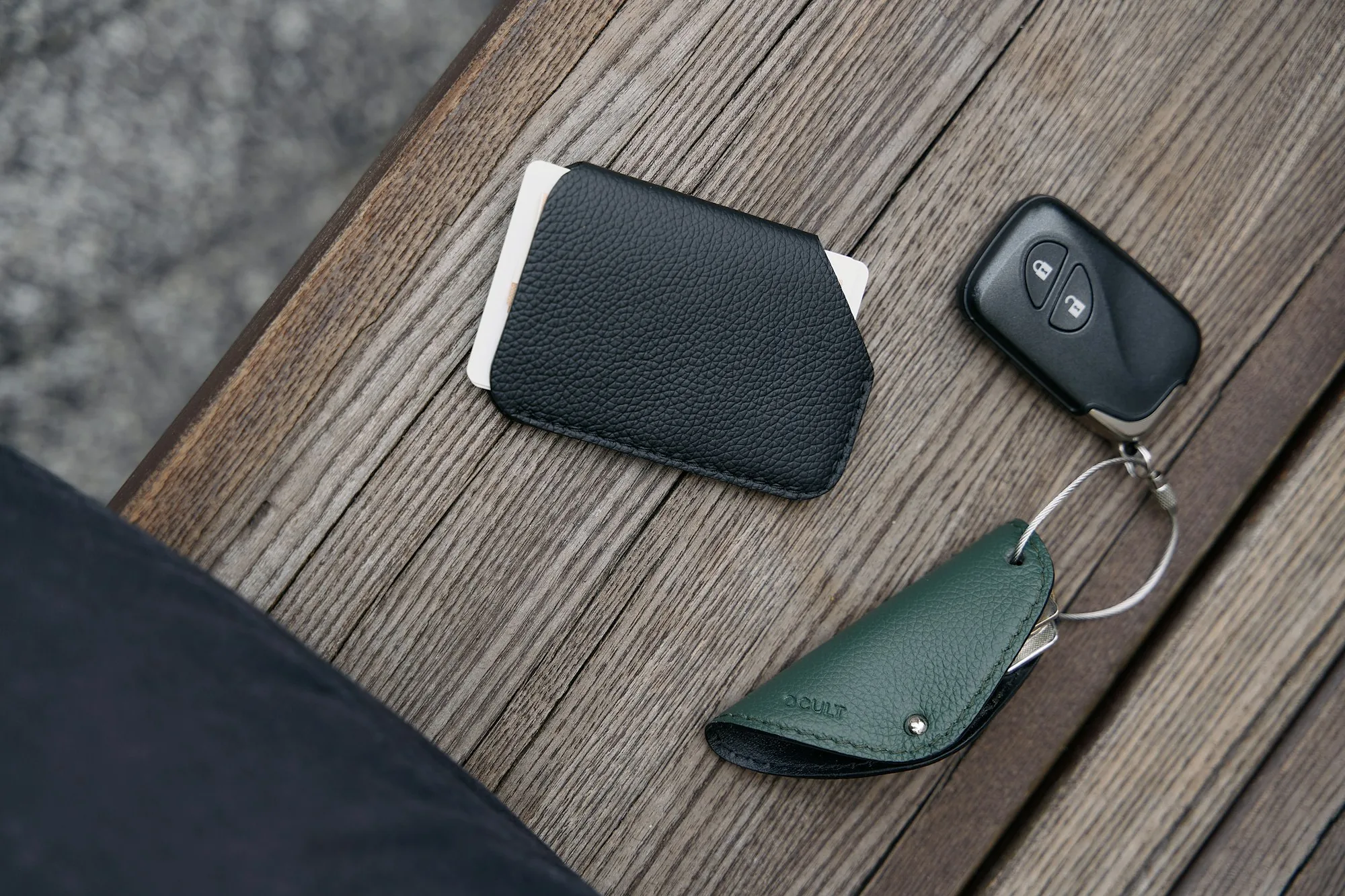 Slim leather wallet holding a card, beside keys on a wooden table
