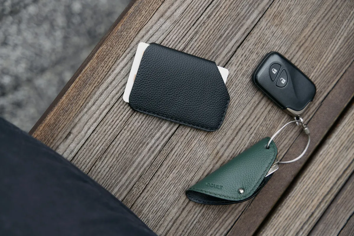 Slim leather wallet holding a card, beside keys on a wooden table