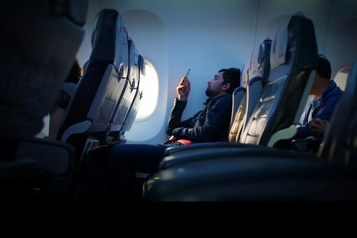 Traveler holding a smartphone beside an airplane window
