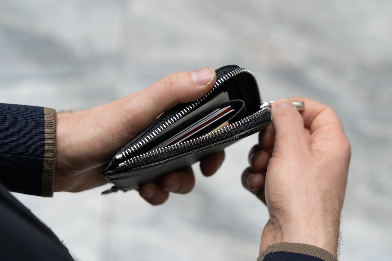 A pair of hands unzipping a black zip-around wallet with the edges of several cards visible inside