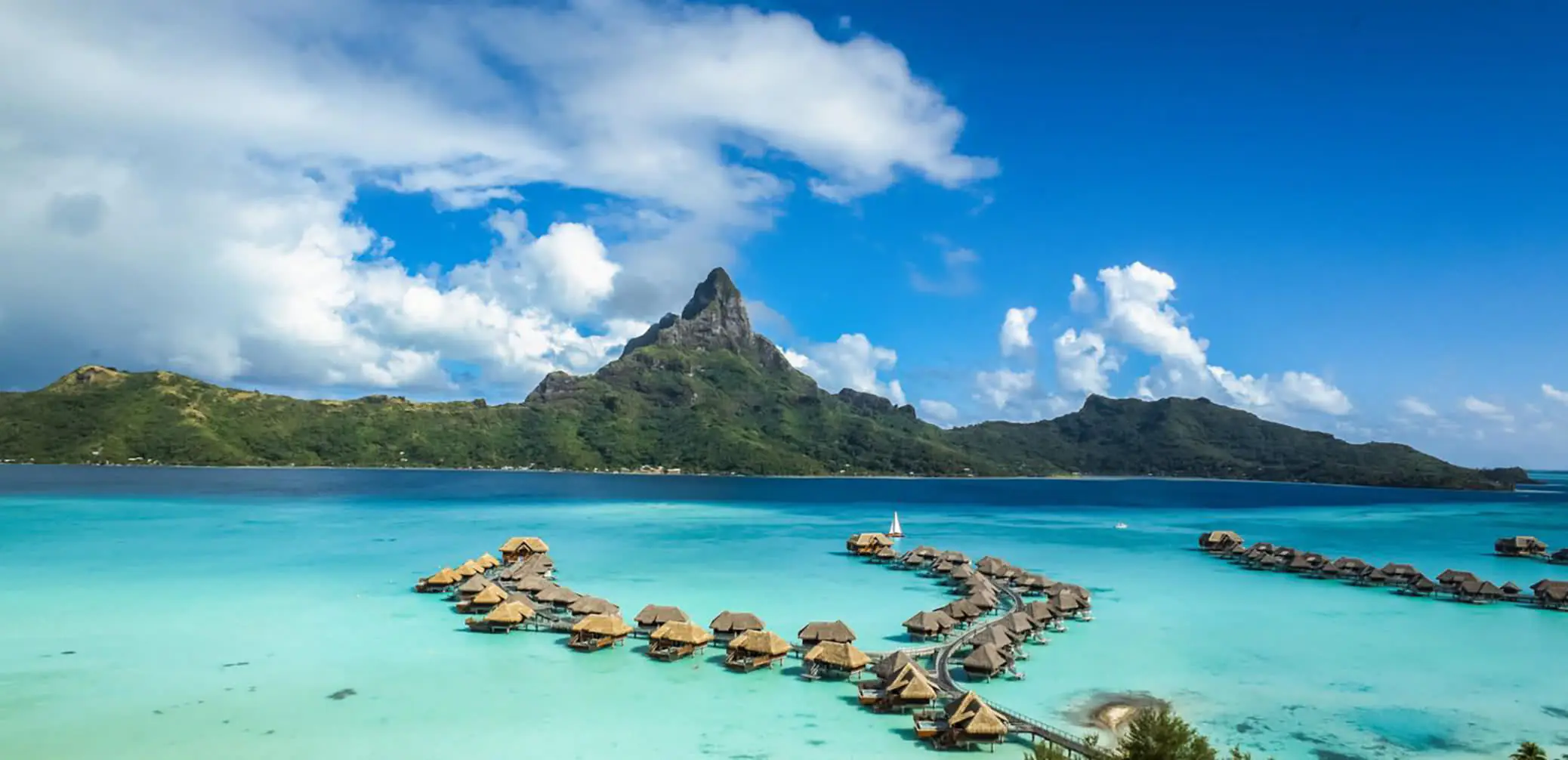 Overwater bungalows in a turquoise lagoon with Mount Otemanu rising behind them in Bora Bora