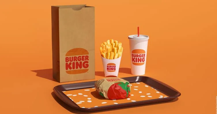 Burger King bag, fries, drink, and wrapped Whopper on a tray against an orange background