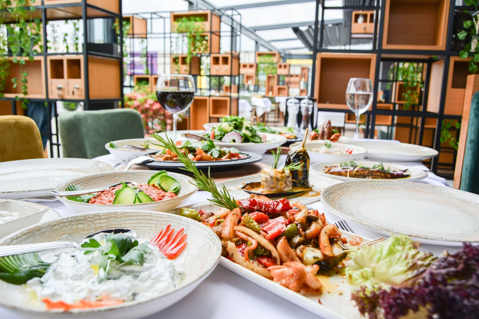 Restaurant table set with shared plates, salads, grilled dishes, and glasses of wine and water