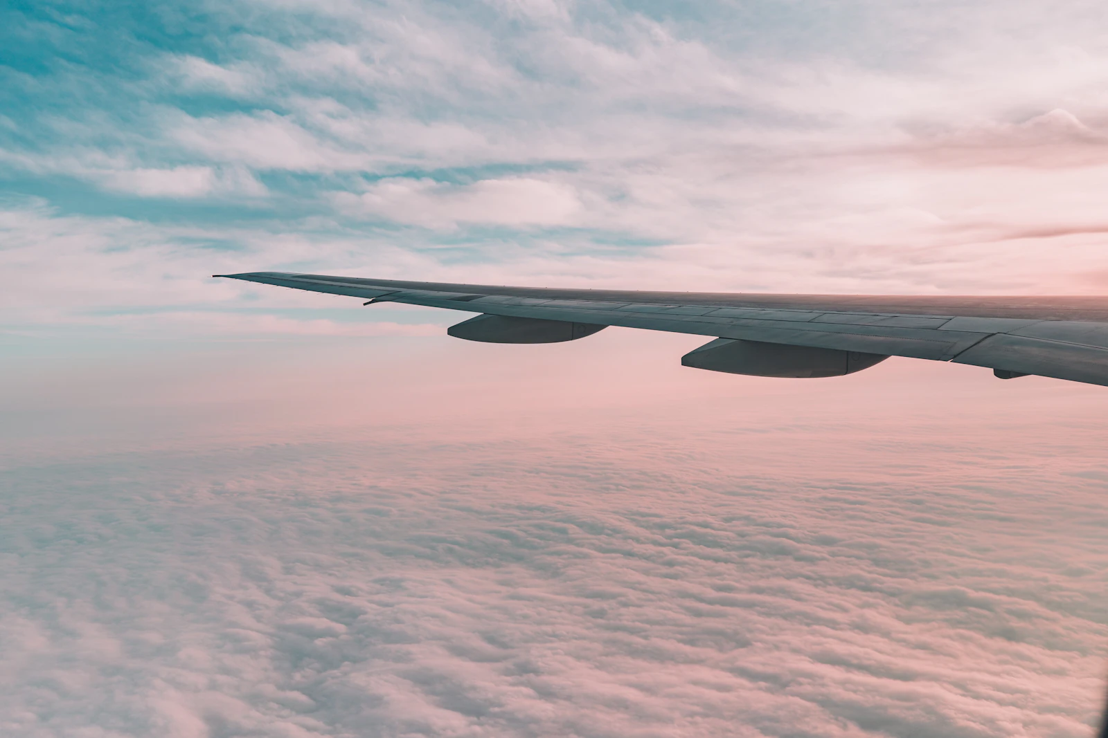 Airplane wing above a layer of pink clouds at sunrise