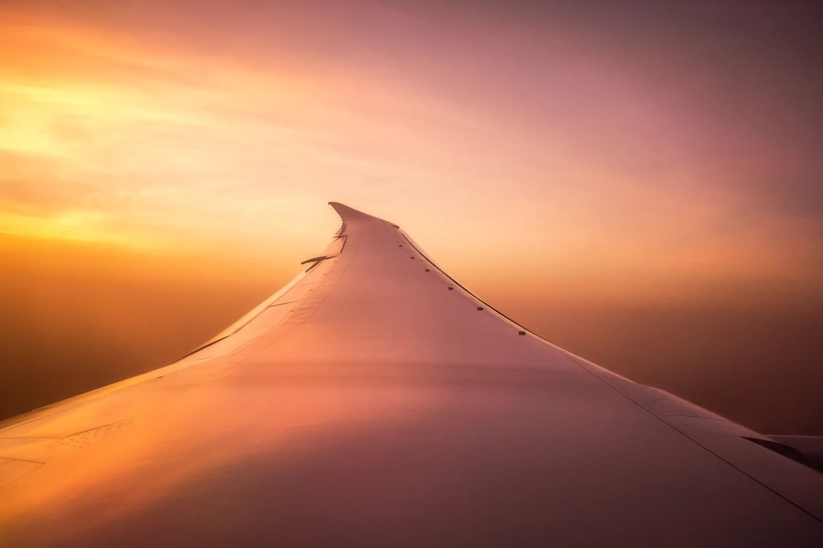 Airplane wing above the clouds at sunset, seen from a passenger window