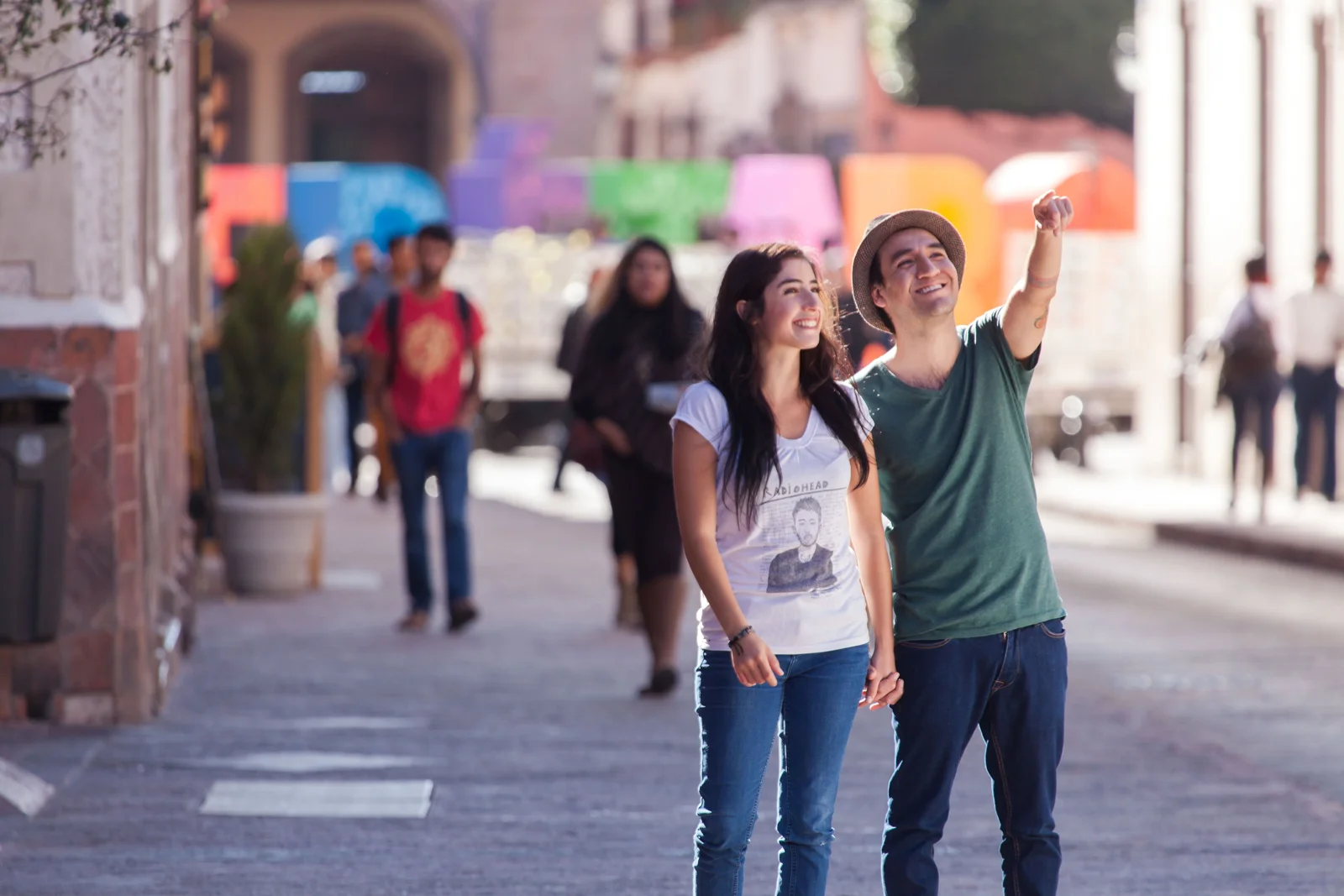 Smiling couple holding hands and pointing at the sights while exploring a sunny, colorful town