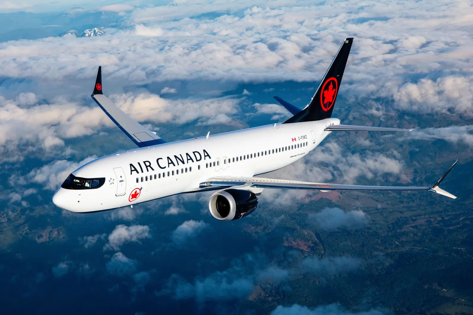 Air Canada Boeing 737 MAX 8 in flight above clouds and forested mountains