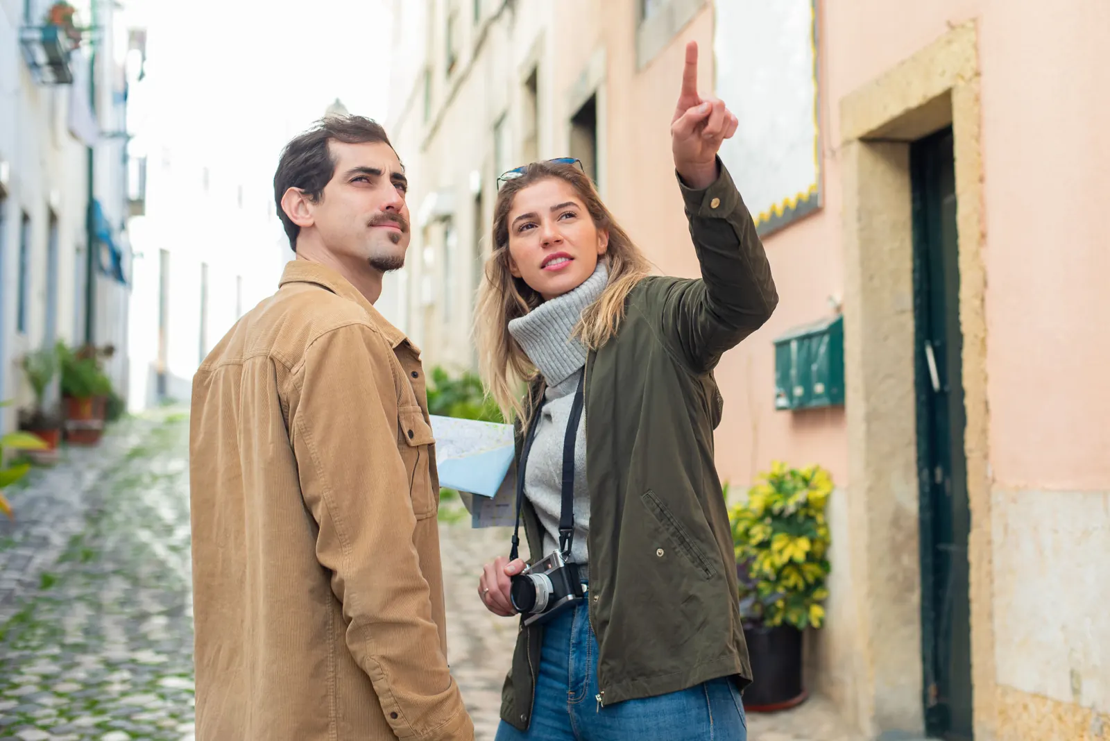 Couple exploring a cobblestone street while traveling, one pointing up at the buildings
