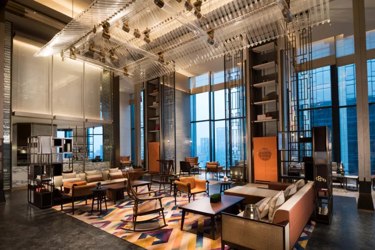 Modern hotel lobby with floor-to-ceiling windows, wood-framed shelving and lounge seating