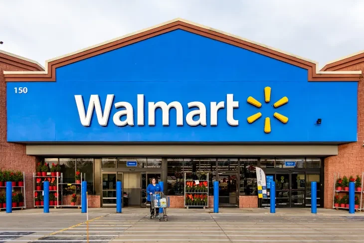 Front entrance of a Walmart store with the blue Walmart sign and a shopper pushing a cart