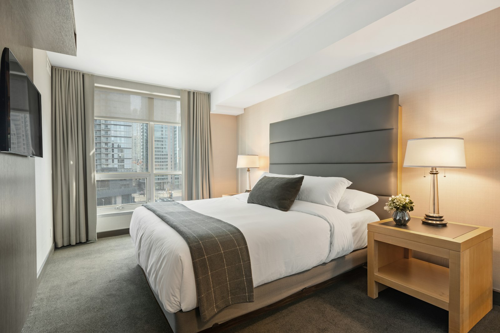 Modern hotel room with a king bed, city view window, and bedside lamps