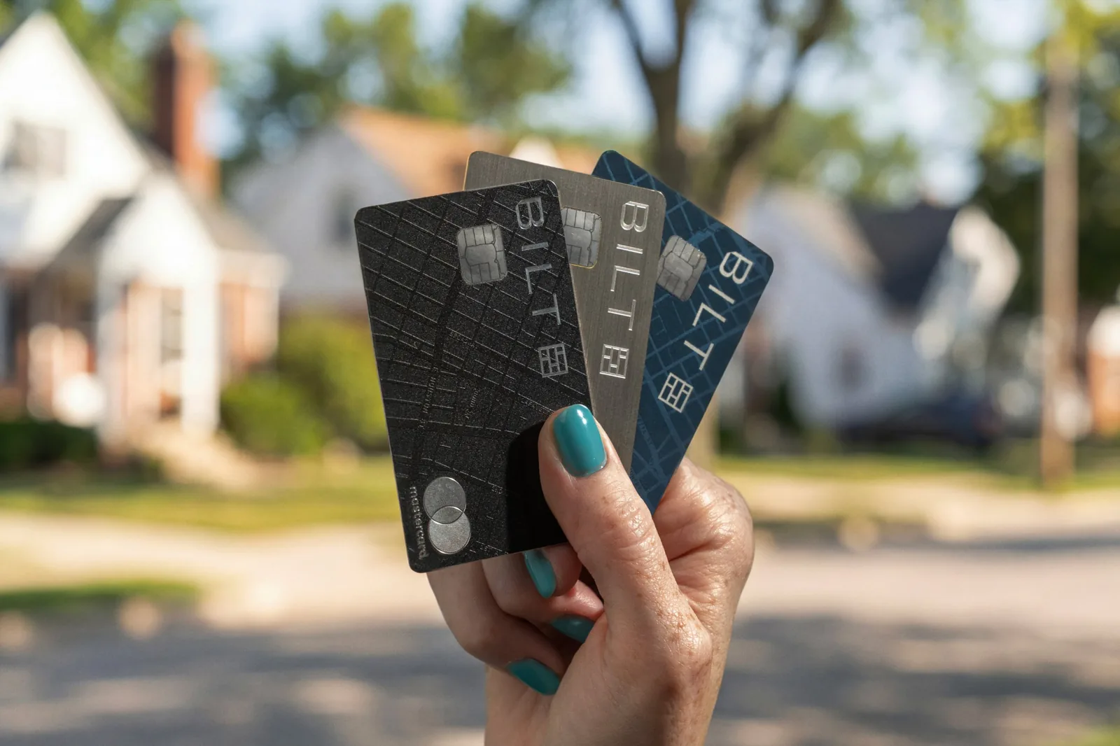 Three Bilt credit cards held up in front of a house