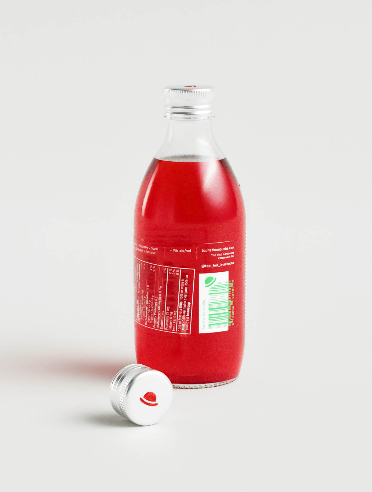 A kombucha bottle shown from the side displays a structured label design integrating a vertical barcode, brand website, and full nutritional facts. The white-on-red text offers strong contrast for legibility, while the design layout keeps all information aligned and clearly organized. The cap, placed neatly beside the bottle, features a red top hat icon, reinforcing brand continuity. This view highlights how design studios handle regulatory and commercial constraints through typographic clarity and effective space management in beverage packaging.