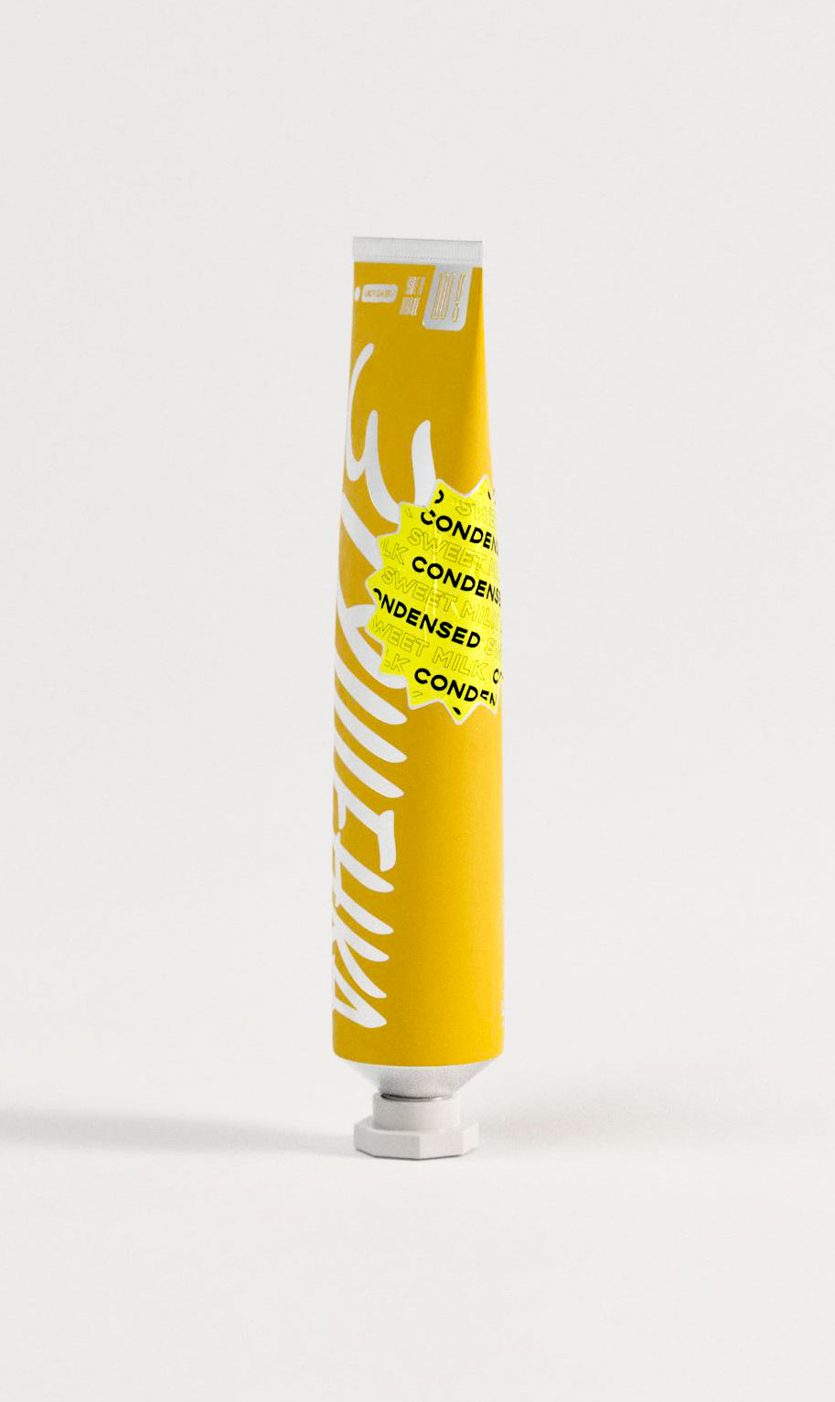 A modern packaging design for condensed milk shown in profile, this yellow squeeze tube includes a neon yellow graphic badge featuring repeated “CONDENSED” and “SWEET MILK” text in various directions. The bold, typographic sticker overlays part of the hand-drawn wordmark running vertically. The visual layering of type and symbol draws on contemporary design aesthetics, referencing zine culture and sticker art, often used in graphic design studio practice to add attitude and cultural reference to everyday products.