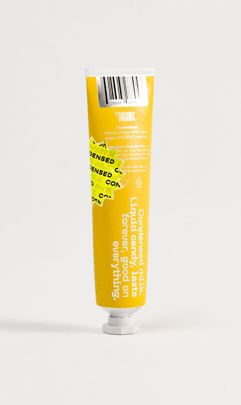 This back-facing view of a condensed milk tube reveals friendly product messaging in clean white type: “Condensed milk. Liquid candy. Lasts forever. Good on everything.” The casual, vertical copy contrasts with the industrial tube form, softened by a bright yellow backdrop. A neon badge overlays part of the back and barcode section, contributing visual play. Ingredient details and organic certification appear at the top. This packaging shows how design studios craft consumer products with personality, combining bold color, witty copy, and compact formatting.